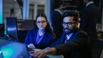 A diverse team of AI developers shares a successful moment in the office. A female programmer smiles as they review the positive results of a complex machine learning algorithm.